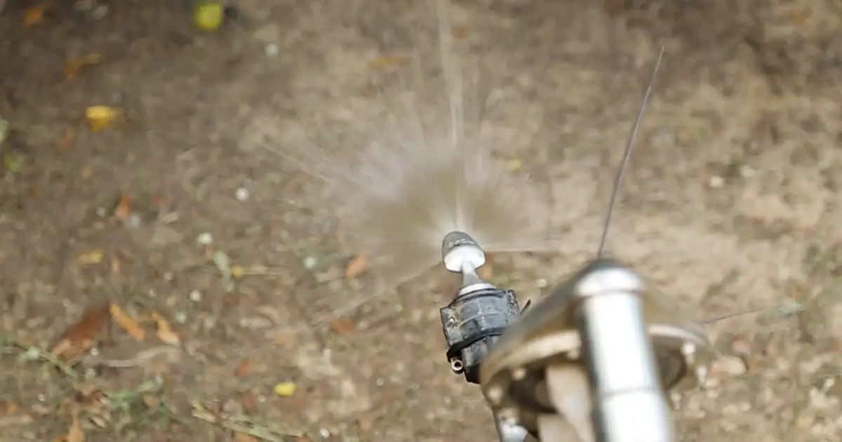 Close-up of a Tow and Fert nozzle applying a fine liquid spray onto orchard soil